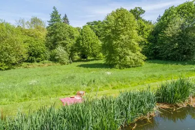 a red object in the grass next to a body of water at Charming cottage in beautiful countryside with a boating lake - The Calf Pens in Ipswich