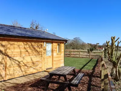 a wooden cabin with a bench next to a fence at Buttercup Lodge in Leiston