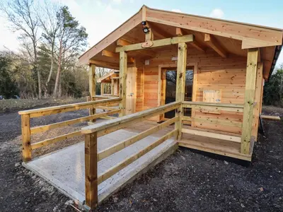 a wooden cabin with a porch and a fence at Buttercup Lodge in Leiston