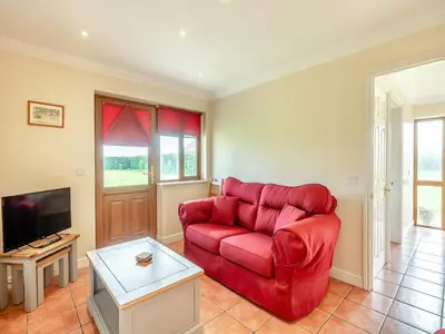 a living room with a red couch and a tv at Orchard Cottage in Saint Osyth