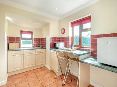 a kitchen with white cabinets and red tiles at Orchard Cottage in Saint Osyth