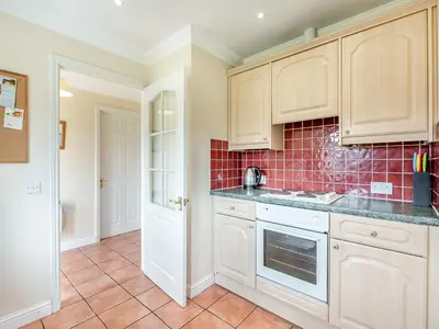 a kitchen with white cabinets and red tile at Orchard Cottage in Saint Osyth