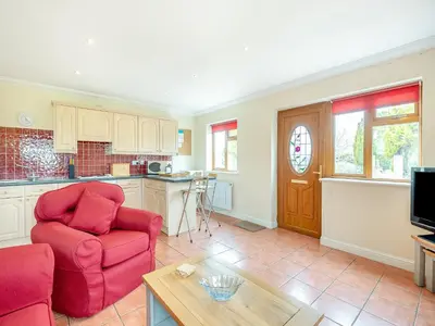 a living room with a red chair and a kitchen at Dairy Cottage in Saint Osyth