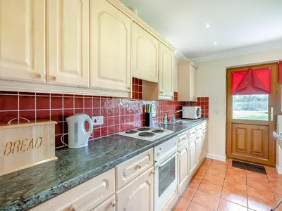 a kitchen with white cabinets and a red tiled wall at Willowtree Cottage in Saint Osyth