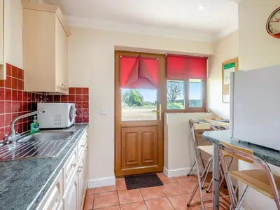 a kitchen with a sink and a door with red curtains at Appletree Cottage in Saint Osyth
