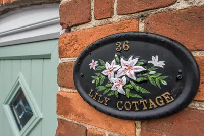 a black sign on a brick wall with pink flowers at Lily Cottage, Leiston in Leiston