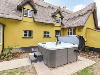 a hot tub in front of a yellow house at The Abbey Cottage in Cockfield