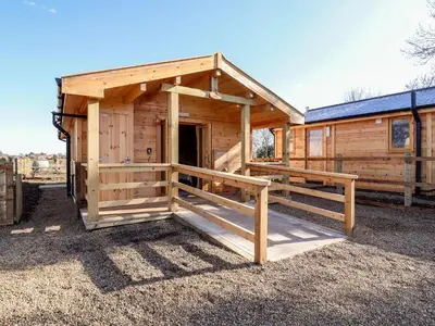 a wooden cabin with a porch and a door at Clover Lodge in Leiston
