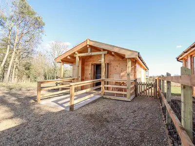 a wooden cabin with a gate and a fence at Clover Lodge in Leiston