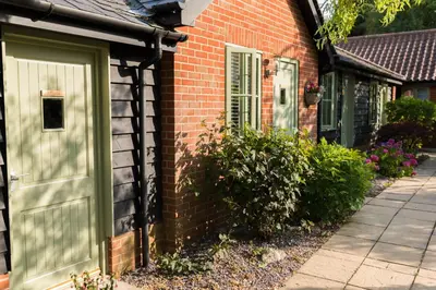 a brick house with a green door and windows at The Foxes Den in Assington