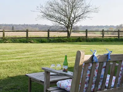 a wooden bench with a picnic table with drinks on it at The Stables in Bealings