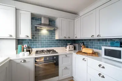 a kitchen with white cabinets and blue tiles at 15 Mill Field - Aldeburgh Coastal Cottages in Aldeburgh