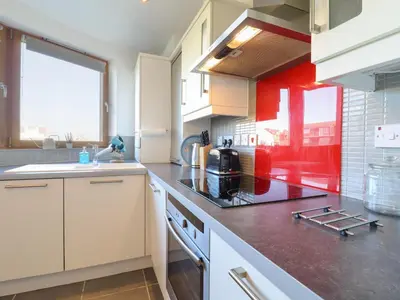 a kitchen with white cabinets and a red wall at Flat 19 By The Beach in Harwich