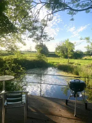 a grill and chairs on a deck next to a river at The Water Shack - Amazing tiny house retreat in Woodbridge