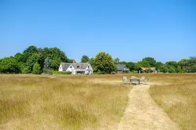 a field with chairs and a house in the background at White Cottage, Iken - Aldeburgh Coastal Cottages in Snape