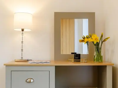 a desk with a vase of flowers and a lamp at Bramley Cottage in North Weald