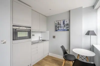 a kitchen with white cabinets and a table and chairs at Luxury Apartment in Chelmsford Bond Street with Sky TV, Movies & Netflix in Chelmsford