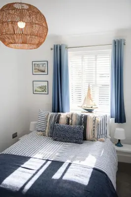 a bedroom with a bed with blue curtains and a window at La Casita - Inside the Gates of Frinton-On-Sea in Frinton-on-Sea
