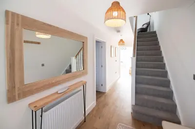 a hallway with a staircase and a mirror on the wall at La Casita - Inside the Gates of Frinton-On-Sea in Frinton-on-Sea
