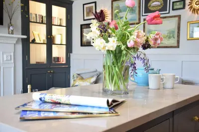 a vase of flowers sitting on a counter with magazines at Cragside, Aldeburgh in Aldeburgh
