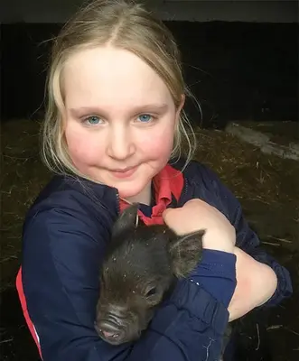 a young girl holding a baby pig in her arms at The Coach House Barn - Valley Farm in Sudbourne