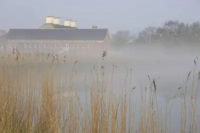 a barn in the fog next to a body of water at The Knox - Beautiful Two Bed Cottage Near Orford in Woodbridge