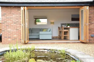 a patio with a couch and a kitchen and a pond at The Knox - Beautiful Two Bed Cottage Near Orford in Woodbridge