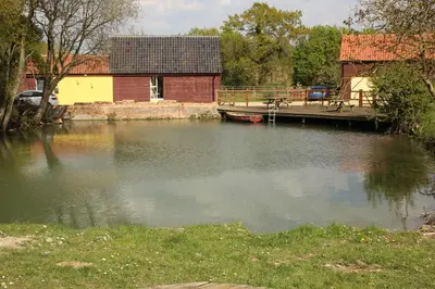 a body of water with a house and a dock at The Tawny Shepherd Hut, Whitehouse Farm in Stowmarket