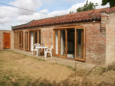 a brick house with a table and chairs on a patio at Haycart Barn in Norwich