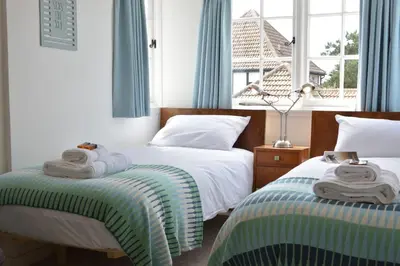 two beds in a bedroom with blue curtains and towels at 4 The Dunes, Thorpeness in Thorpeness