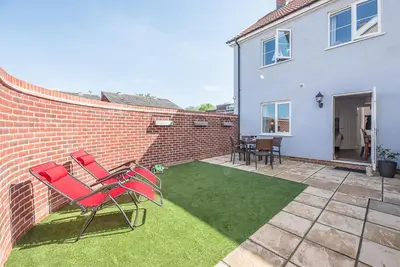 a patio with red chairs and a brick wall at Alde Seagull, Aldeburgh in Aldeburgh