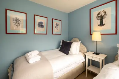two beds in a blue room with pictures on the wall at Quay Cottage - Aldeburgh Coastal Cottages in Aldeburgh
