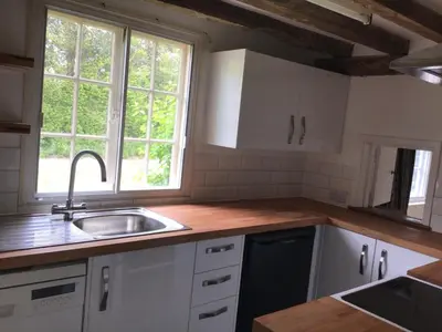 a kitchen with white cabinets and a sink and two windows at Thatched Cottage in Wix