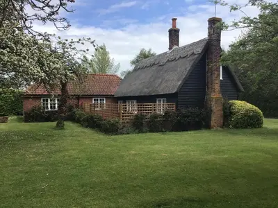 an old house with a thatched roof in a yard at Thatched Cottage in Wix