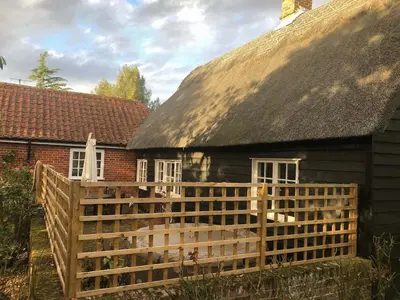 an old house with a wooden fence in front of it at Thatched Cottage in Wix