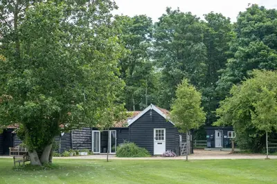a black cabin with a white door and a tree at The Cart Lodge - Aldeburgh Coastal Cottages in Wickham Market