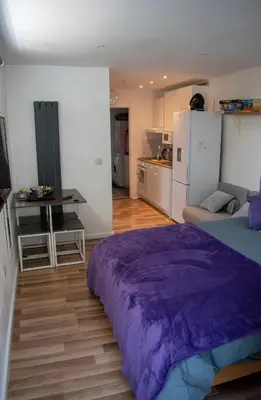 a bedroom with a purple bed and a kitchen at 121 Studio - Apartment with Kitchen, Terrace, Stansted Airport Shuttle in Bishops Stortford