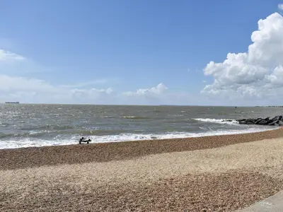 a person sitting on a bench on the beach at Beach View Cottage in Felixstowe