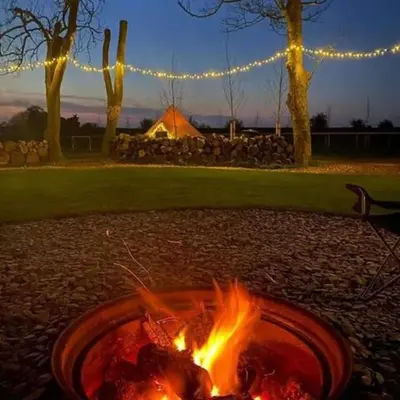 a fire pit in a park with a tent in the background at Willow Grove Farm Glamping in Lakenheath