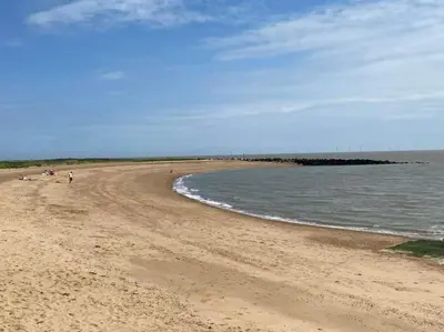 a beach with people walking on the sand and water at Lodge Sleeps 8- Parking Wifi Campsite Amenities in Jaywick Sands