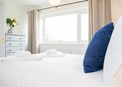 a bedroom with a bed with blue pillows and a window at Parkside House Stevenage in Stevenage