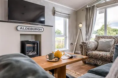 a living room with a fireplace and a table at Marshwiggle, Aldeburgh in Aldeburgh