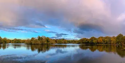 a large lake with trees and a cloudy sky at Modern Studio with parking in shared garden in Theydon Bois