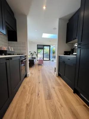 a kitchen with black cabinets and a wooden floor at Modern Studio with parking in shared garden in Theydon Bois