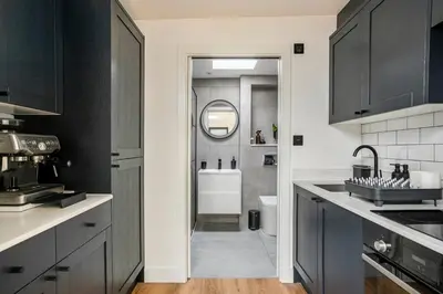 a kitchen with black cabinets and a bathroom with a sink at Modern Studio with parking in shared garden in Theydon Bois