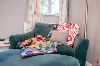 a green chair with a blanket and a pillow on it at Ferry Corner Cottage, Sudbourne in Woodbridge