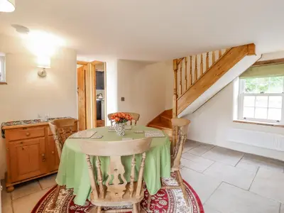 a dining room with a table and a staircase at Postbox Cottage in Thetford