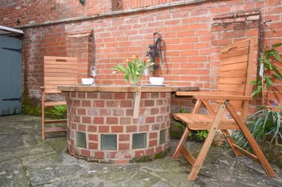 a brick wall with a table and a wooden chair at Chapel Cottage, Newbourne in Newbourn