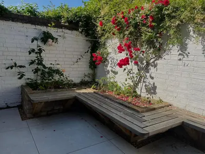 a wooden bench with red flowers on a brick wall at 300m to Fitzwilliam museum 3 en-suites double bedroom Victoria house in Cambridge
