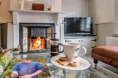 a man sitting in a living room with a fireplace at Periwinkle Cottage, Aldeburgh in Aldeburgh